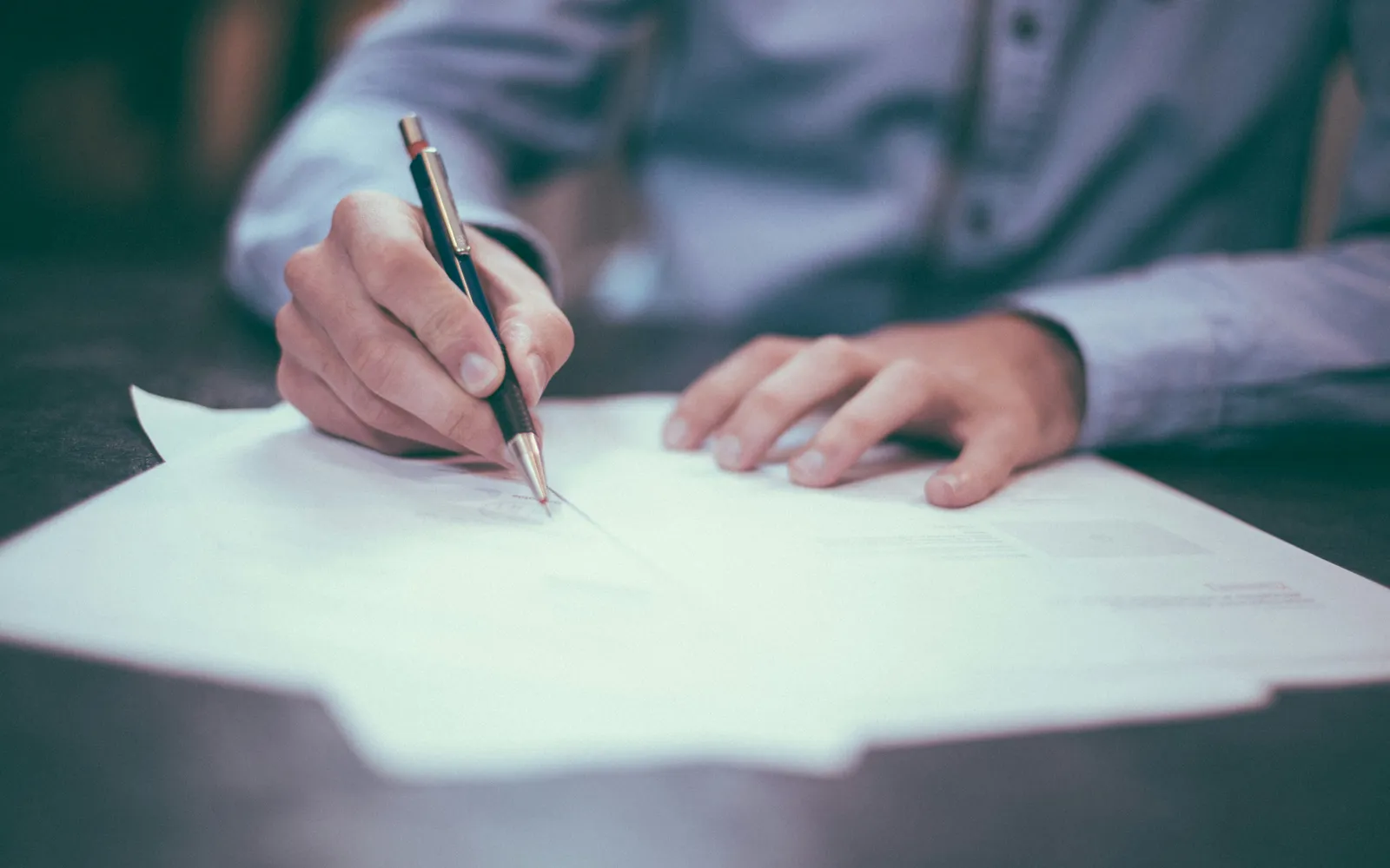 Une personne relit et annote un document sur une table.